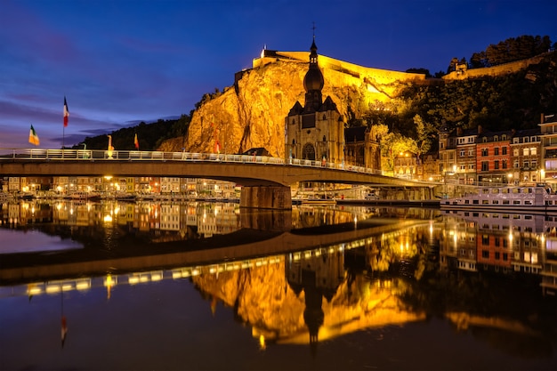 Visão noturna da cidade de Dinant, Igreja Colegiada de Notre Dame de Dinant sobre o rio Meuse e a ponte Pont Charles de Gaulle e Dinant Citadel iluminada à noite. Dinant, Bélgica