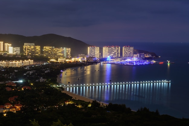 Visão noturna da cidade de Sanya com edifícios, estruturas, estradas, calçadas, postes, pontes de iluminação multicolorida. Sanya, Hainan, China