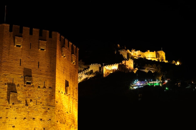 Visão noturna da Torre Vermelha (Kizil Kule) e da antiga parede de pedra do Castelo de Alanya, Turquia