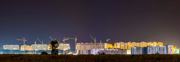 Visão noturna de panorama de muitos guindastes de construção no canteiro de obras da nova área residencial moderna