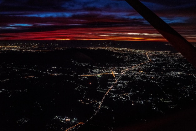 Visão noturna do avião a jato no crepúsculo com o céu vermelho e a luz da cidade