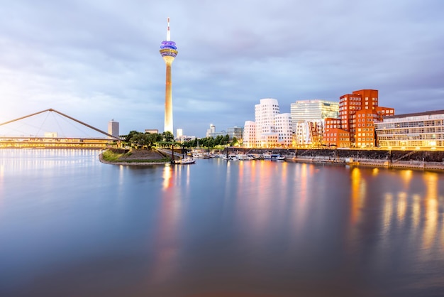 Visão noturna no rio Rhein com edifícios iluminados e torre de televisão na cidade de Dusseldorf, Alemanha