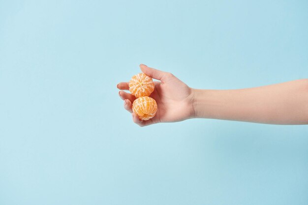 Visão recortada da mulher segurando tangerinas descascadas na mão isoladas em azul