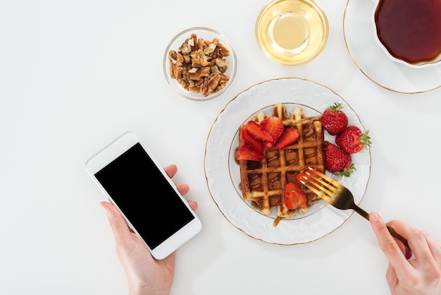 Visão recortada da mulher tomando café da manhã e segurando smartphone em branco