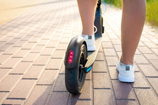 Visão recortada das pernas do homem e scooter elétrico no estilo de vida urbano de rua da cidade