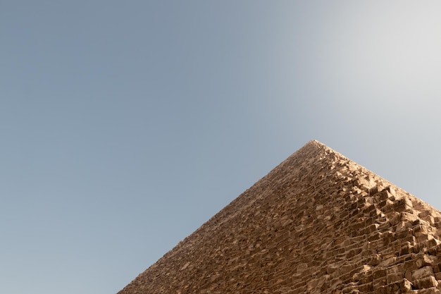 Visão recortada de baixo ângulo da grande pirâmide de gizé com céu azul claro e espaço para cópia com raio de sol em