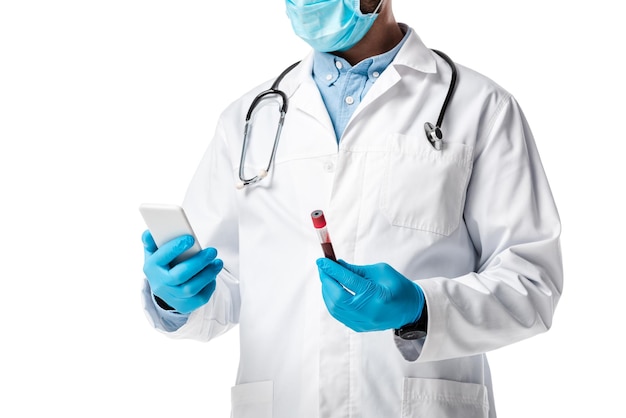 visão recortada de médico com máscara médica e casaco branco segurando smartphone e tubo de teste com sangue