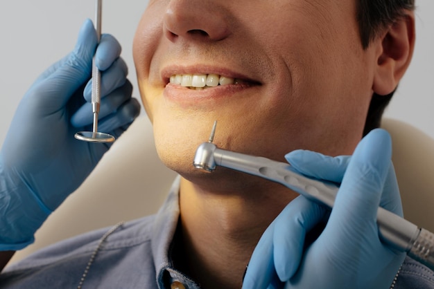 Visão recortada do dentista em luvas de látex segurando instrumentos dentários perto de paciente alegre