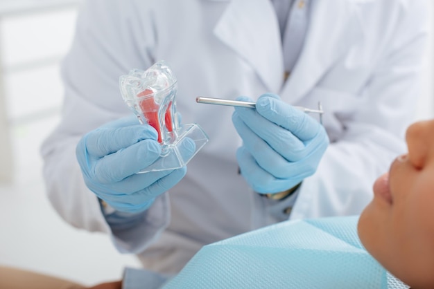 Visão recortada do dentista segurando instrumento dental modelo de dente puro e paciente afro-americano