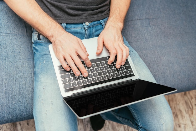 Visão recortada do homem em jeans digitando no laptop com vista superior de tela em branco