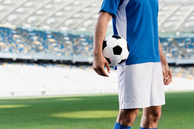 Visão recortada do jogador de futebol profissional em uniforme azul e branco com bola no campo de futebol em