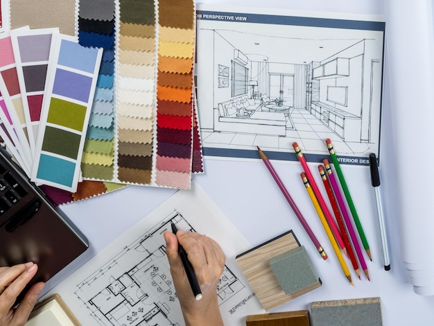Visão superior das mãos de arquitetos desenhando uma casa moderna com amostra de material na mesa criativa