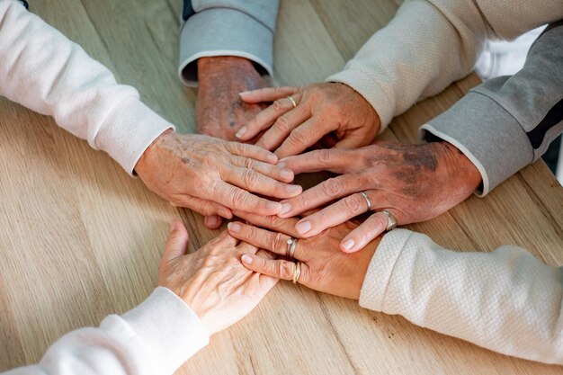 Visão superior das mãos de três idosos colocados em círculo mostram unidade e apoio juntos na superfície de madeira