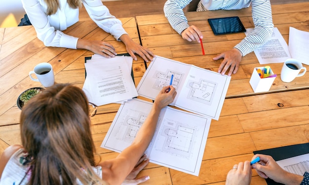 Visão superior de arquitetos em uma reunião de trabalho olhando desenhos de construção de uma casa