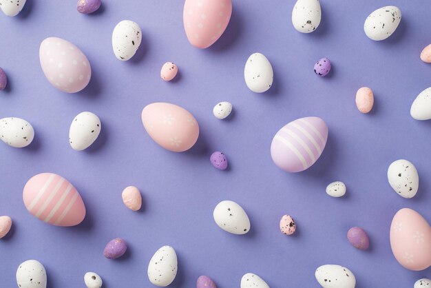 Visão superior de muitos ovos de Páscoa multicoloridos de tamanho diferente com listras e pontos no fundo isolado violeta pastel