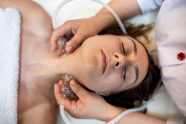 Visão superior de uma massagista profissional massageando o rosto de uma jovem cliente em um centro de spa de saúde o conceito de beleza uma atmosfera de paz e relaxamento face close-up