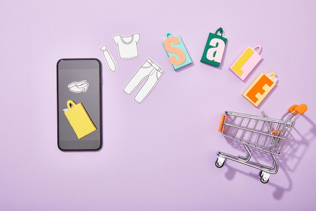 Visão superior do smartphone perto de sacolas de compras com letras de venda e corte de papel de roupas caindo