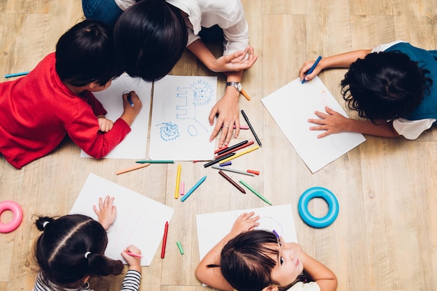 Visão superior Grupo de crianças felizes da família garoto menino e menina pintura de jardim de infância desenhando em peper com educação de professores juntos na sala de jogos interior