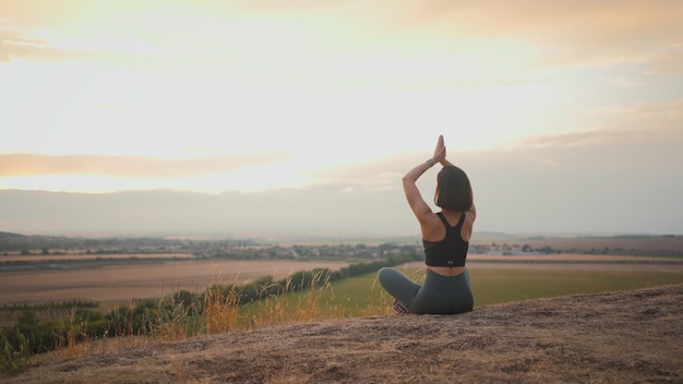 Visão traseira da mulher morena calma meditando e sentada em pose de lótus na natureza