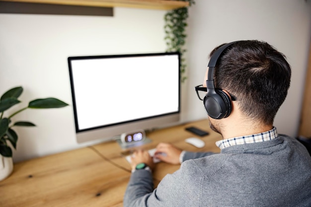 Visão traseira de um homem com tipos de fones de ouvido no teclado e trabalhando em home office