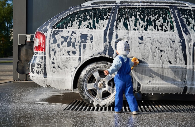 Visão traseira de uma criança do sexo masculino aprendendo a lavar o carro com sabão na lavagem de carros