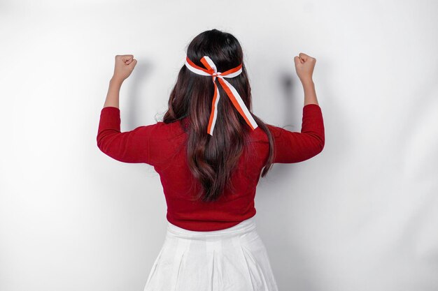 Visão traseira de uma jovem asiática com um gesto feliz e bem-sucedido usando top vermelho e faixa de bandeira isolada por fundo branco Conceito de dia da independência da Indonésia39