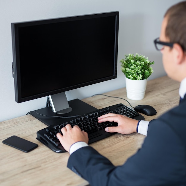 Visão traseira do homem de negócios usando computador no espaço de cópia do escritório na tela em branco