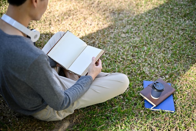 Visão traseira Focado jovem estudante universitário asiático lendo um livro relaxando no parque do campus