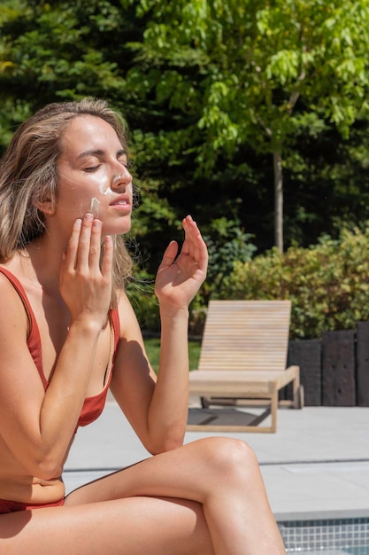 Visão vertical da jovem gorgeour com corpo real, colocando creme solar facial enquanto fecha os olhos sob o sol