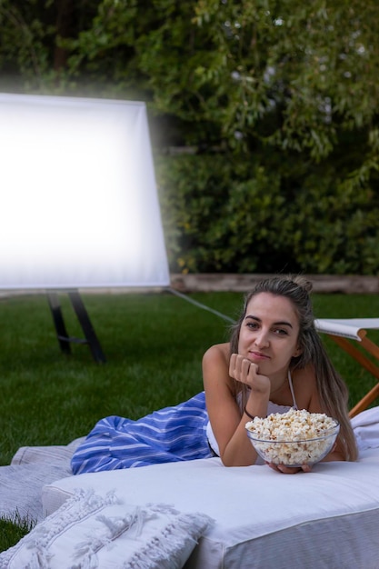 Foto visão vertical da jovem linda olhando para a câmera com uma tigela cheia de pipocas no cinema ao ar livre