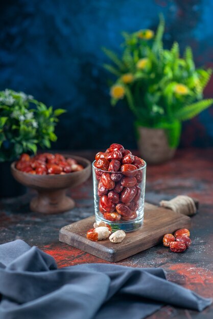 Visão vertical de frutas frescas de amora-prateada dentro e fora de um vidro em uma tábua de madeira e um vaso de flores no fundo da mistura de cores