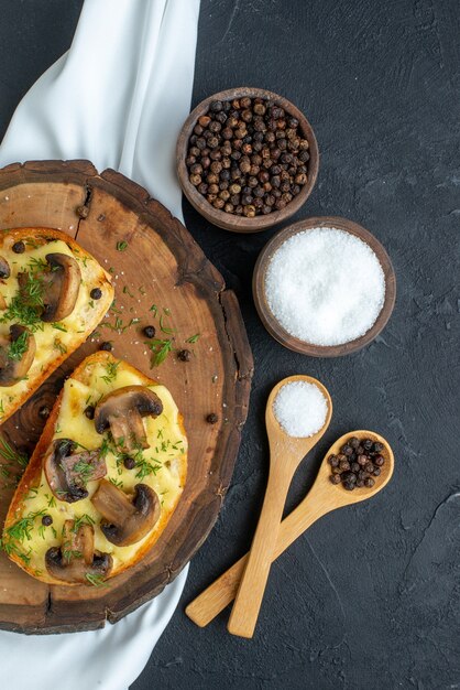 Visão vertical de um delicioso lanche com cogumelos na placa de madeira e especiarias na toalha branca sobre fundo preto