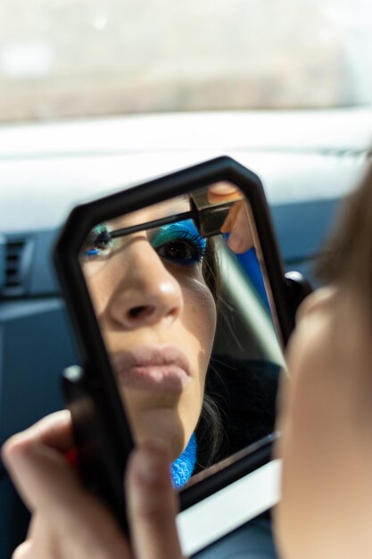 Visão vertical de um reflexo de espelho de uma mulher aplicando maquiagem em um carro maquiagem de olhos com tons azuis