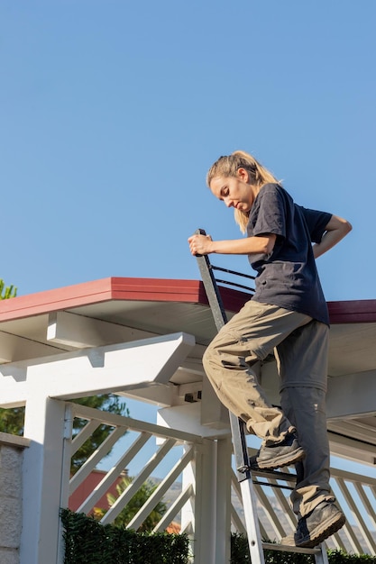 Visão vertical de uma jovem trabalhadora em uma escada entrando no telhado com céu azul claro