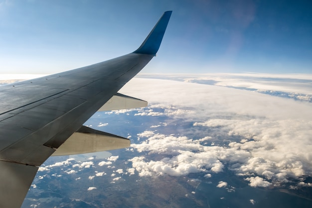 Visión desde el aeroplano en el ala blanca del avión que vuela sobre paisaje nublado en mañana soleada. Concepto de transporte y transporte aéreo.