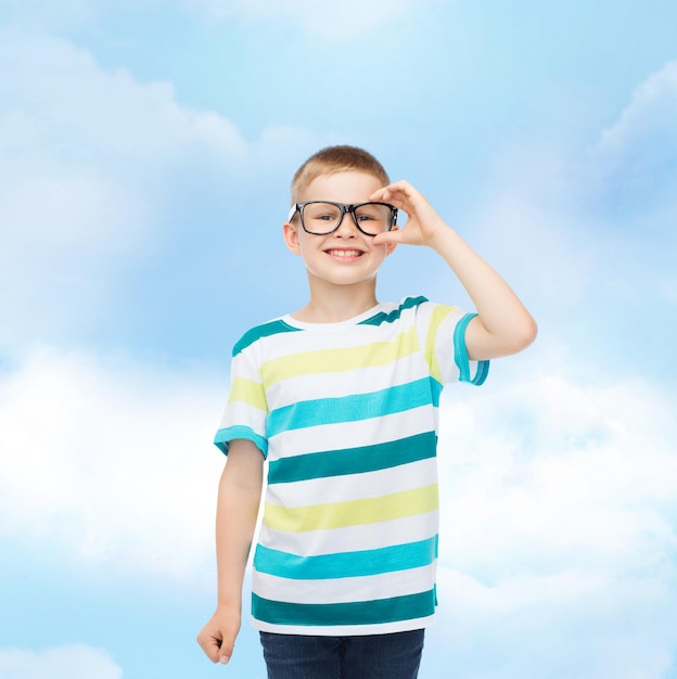 Vision, Bildung, Kindheit und Schulkonzept - lächelnder kleiner Junge mit Brille über blauem Himmel mit weißem Wolkenhintergrund