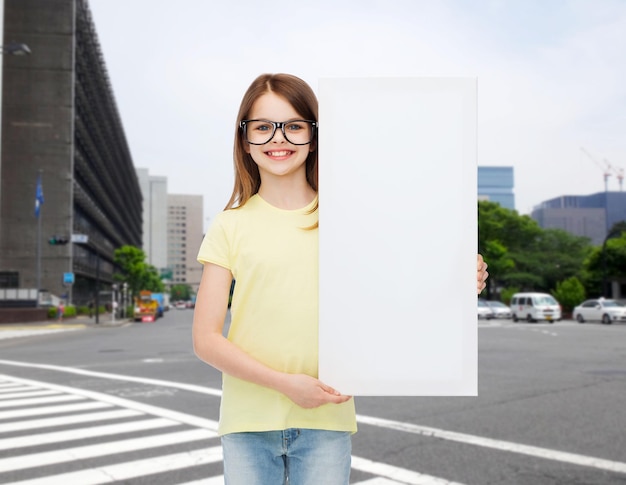 visión, salud, publicidad y concepto de personas - niña sonriente que usa anteojos con tablero blanco en blanco