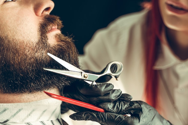 Visita à barbearia. o mestre faz um corte de barba com tesoura