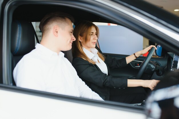 Visita al concesionario de automóviles. Hermosa pareja está mirando a la cámara y sonriendo mientras está sentado en su auto nuevo