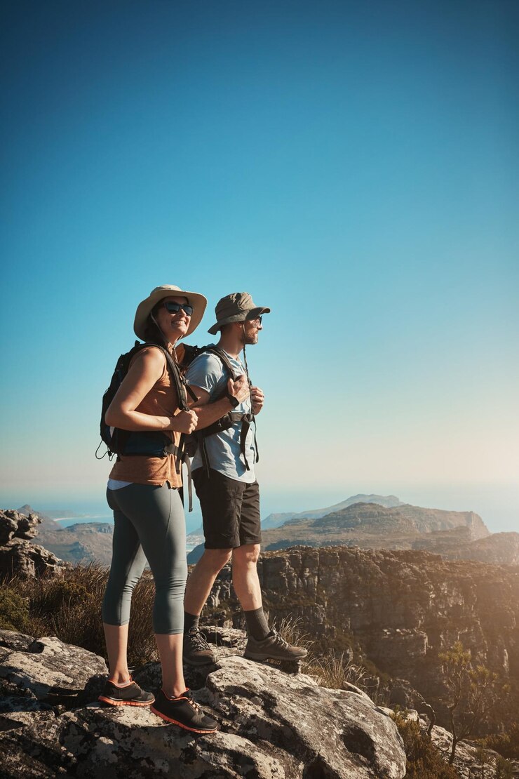 Foto visita a la montaña y pareja feliz en la montaña con aptitud para la aventura, senderismo por acantilados y mochila, viajes por senderos naturales y personas para el bienestar y el ejercicio, logros en vacaciones de entrenamiento o viajes.