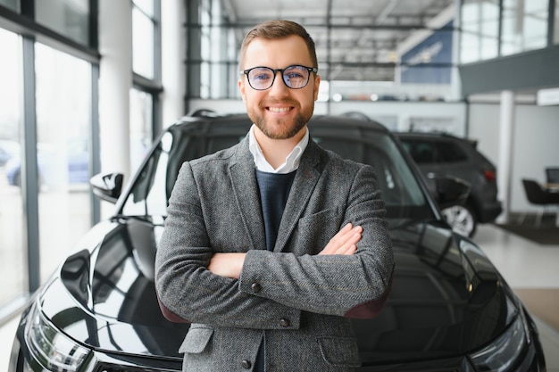 Visitando a concessionária de carros Bonito homem barbudo está acariciando seu carro novo e sorrindo