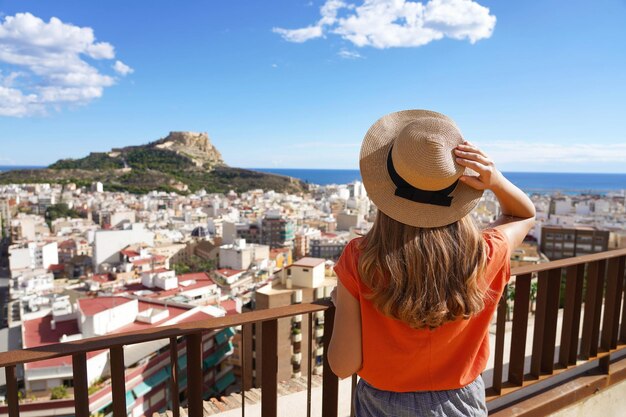 Visitando Alicante en España. Chica viajero disfrutando de la vista del paisaje urbano de Alicante y el Monte Benacantil con el Castillo de Santa Bárbara y el mar de fondo. Joven turista visitando el sur de Europa.