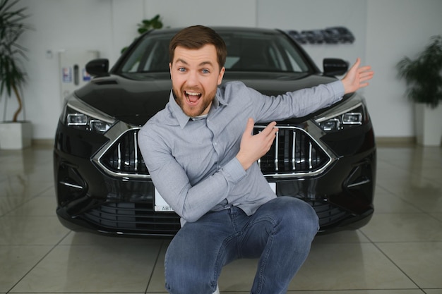 Visitando el concesionario de automóviles Un hombre guapo con barba está acariciando su auto nuevo y sonriendo