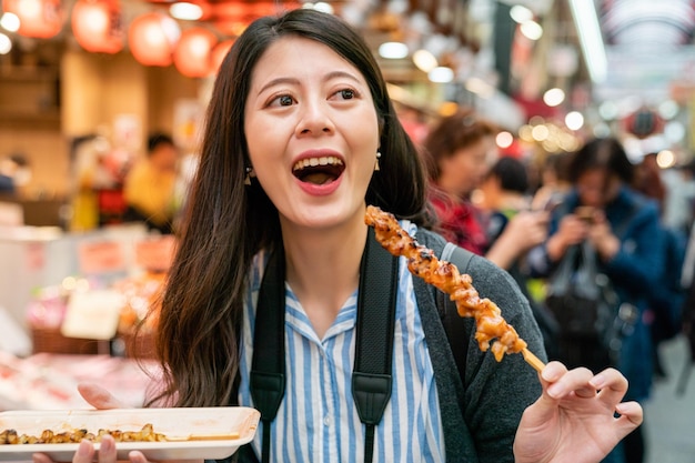 visitante asiática feliz con su comida. una especie de cocina japonesa yakitori. disfrutándolo con pura satisfacción