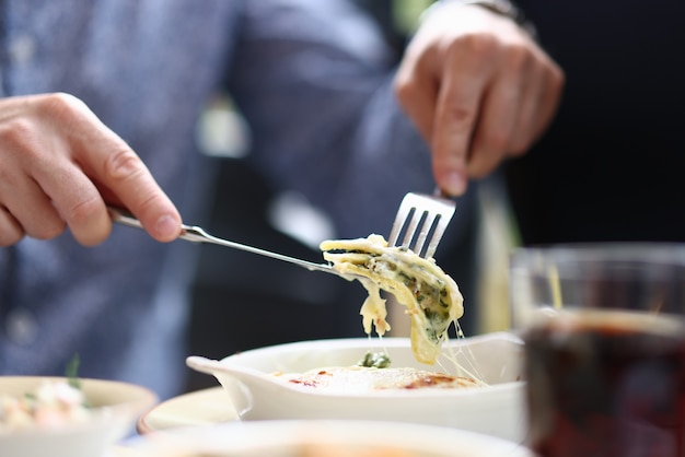 Visitante de bistró sentado en la mesa sosteniendo un tenedor y un cuchillo con un trozo de boloñesa