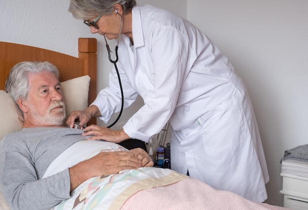 Visitante de saúde e um homem barbudo idoso na cama durante a visita domiciliar