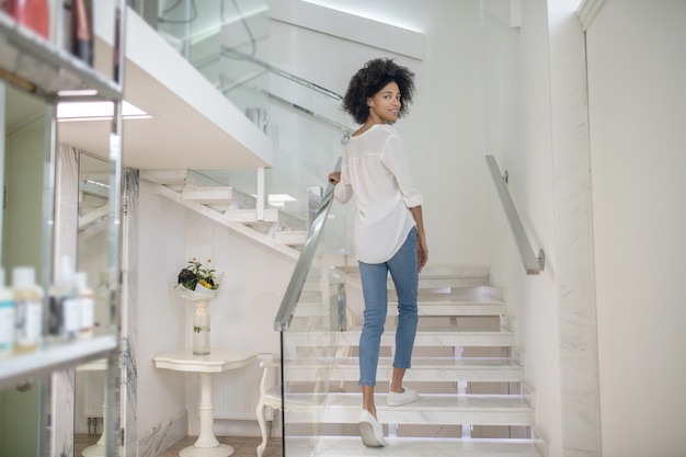 Visitar. Mujer joven con cabello rizado oscuro mirando hacia atrás subir escaleras en el centro de cometología