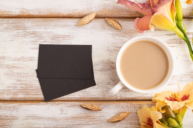 Visitenkartemodell des schwarzen Papiers mit orange Taglilienblume und Tasse Kaffee auf Draufsicht-Kopienraum des weißen hölzernen Hintergrundes