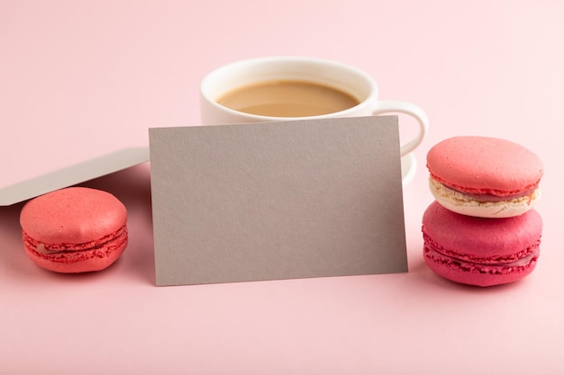 Visitenkartenmodell aus grauem Papier mit roten und violetten Makronen und einer Tasse Kaffee auf rosa Pastellhintergrund, Seitenansicht, Kopienraum
