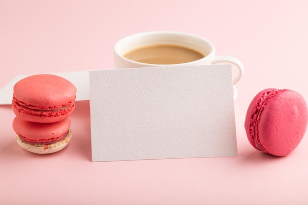 Visitenkartenmodell aus weißem Papier mit roten und violetten Makronen und einer Tasse Kaffee auf rosa Pastellhintergrund, Seitenansicht, Kopienraum